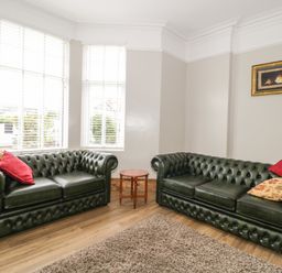 A living room with two green leather sofas with cushions and a small wooden table between them at 23 Carmen Sylva Road in Llandudno