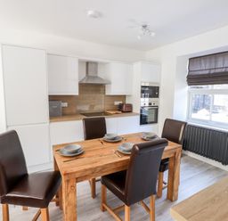 A kitchen with a wooden dining table set with four place settings and four brown chairs at 8 Waterhead Terrace Ambleside