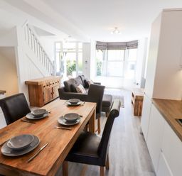 A kitchen and dining area with wooden table and chairs next to a living room with a sofa and large windows at 8 Waterhead Terrace Ambleside