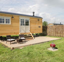 A wooden cabin on wheels with outdoor chairs and table on a gravel patio and grills on grass at Waylands in Uffington