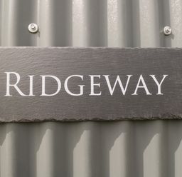 A slate sign with the word Ridgeway mounted on a corrugated metal wall at Ridgeway in Uffington