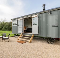 An outdoor seating area with two chairs and a small table next to a grey corrugated metal shepherds hut with open double doors at Ridgeway in Uffington