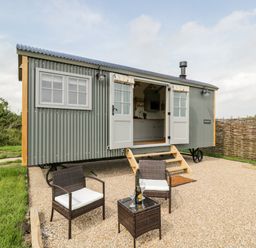A small grey corrugated metal cabin with open French doors and two chairs with a table outside at Ridgeway in Uffington