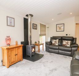A living room with a wood stove and leather sofas with deer cushions at Robin Lodge in Cartmel