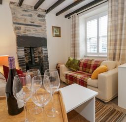 A living room with a stone fireplace a bottle of wine and wine glasses on a tray at Dolwen in Penmachno