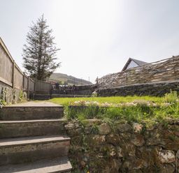 A garden with stone steps leading to a grassy area with a table and chairs behind a wooden fence at Dolwen in Penmachno