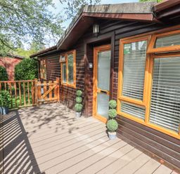 A wooden deck outside a cabin with potted plants and a wooden gate at Grizedale Lodge Langdale 18 White Cross Bay near Windermere