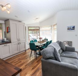 An open plan room with a kitchen area sink and cabinets a dining table with green chairs and a gray sofa at Grizedale Lodge Langdale 18 White Cross Bay near Windermere
