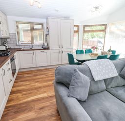 An open kitchen and dining area with white cabinets wooden countertops a grey sofa and green dining chairs at Grizedale Lodge Langdale 18 White Cross Bay near Windermere