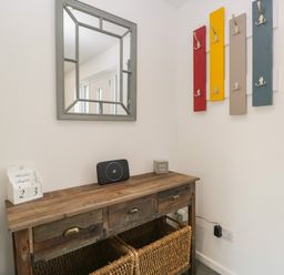A hallway with a wooden console table baskets mirror and colorful coat hooks at 26 Hycemoor Way Bootle Near Millom