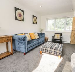 A living room with a blue sofa and plaid ottoman at 26 Hycemoor Way Bootle Near Millom