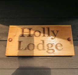 A wooden sign with the text Holly Lodge mounted on a dark wooden surface at Holly Lodge in Liverton