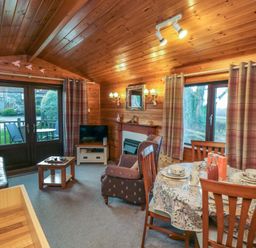 A wooden living room with a dining table set curtains a sofa chairs and a television at Holly Lodge in Liverton