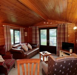 A living room with wood-paneled walls and ceiling with sofas and armchairs around a coffee table at Holly Lodge in Liverton