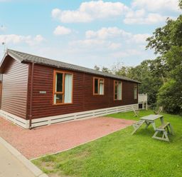 A wooden lodge with several windows a gravel driveway and a picnic table on the grass at Number 43 Burnside Lodge in Felton