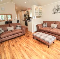 A living room with two brown sofas a plaid ottoman a dining table and kitchen area at Number 43 Burnside Lodge in Felton