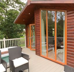 An outdoor deck with black wicker chairs cushions a hot tub and large windows of a wooden cabin at Number 43 Burnside Lodge in Felton