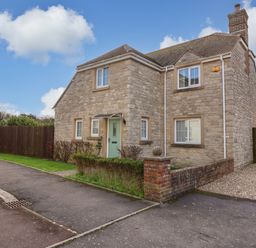 A stone house with a green front door and multiple windows next to a paved sidewalk at West Bay Holiday Home in West Bay
