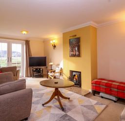 A living room with sofas a round table a TV on a stand a fireplace and a red plaid bench at West Bay Holiday Home in West Bay