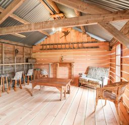 A wooden room with stools a table a loveseat and a wicker chair at Y Caban in Pontfadog near Llangollen