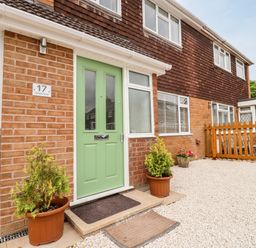 Exterior of house with green front door two potted plants gravel yard and wooden fence at 17 Sands Close in Broadway