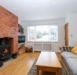 A living room with a brick fireplace a wooden coffee table and sofa with cushions at 17 Sands Close in Broadway