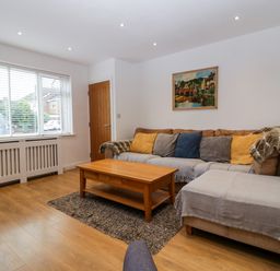 A living room with a sectional sofa with cushions a wooden coffee table a rug and a wall painting at 17 Sands Close in Broadway