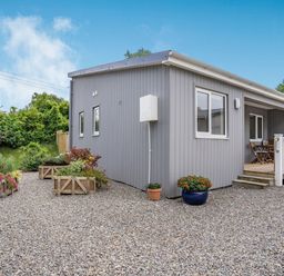 A gray wooden lodge with gravel ground and potted flowers at Caldey Lodge (Bier Wood Lodges) in Manorbier