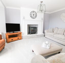 A living room with a television on a wooden stand a fireplace a beige sofa a brown armchair and a large ottoman at 12 Claremont Falls Polperro