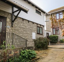 An exterior view of stone houses with plants and a paved walkway at 12 Claremont Falls in Polperro