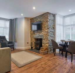 A living room with a stone fireplace and a wall-mounted TV next to a round dining table with chairs at Lower Sheriff's Place in Windermere
