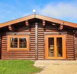 A log cabin with wooden framed window and glass double doors on grass and gravel at Oak Lodge in Greetham Rutland