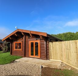 A wooden log cabin with glass doors and a wooden fence in a grassy area at Oak Lodge in Greetham Rutland