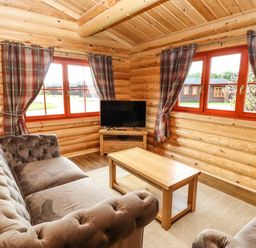 A living room with two sofas a wooden coffee table a TV on a stand and windows with patterned curtains at Oak Lodge in Greetham Rutland