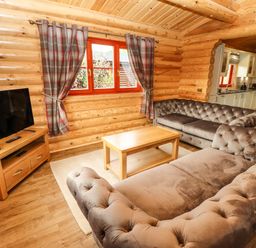 A living room with tufted sofas, wooden coffee table, television on wooden stand, and window with plaid curtains at Oak Lodge in Greetham Rutland