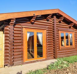 A wooden log cabin with glass double doors and a window at Holly Lodge in Greetham Rutland