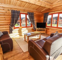 A living room with brown leather sofas a wooden coffee table a television and plaid curtains at Holly Lodge in Greetham Rutland