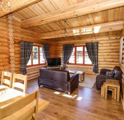A living room with wooden walls and ceiling brown leather sofas wooden dining table and chairs and windows with plaid curtains at Pine Lodge in Greetham Rutland