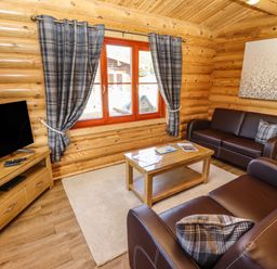 A living room with leather sofas a wooden coffee table a television on a wooden stand and plaid curtains at Pine Lodge in Greetham Rutland