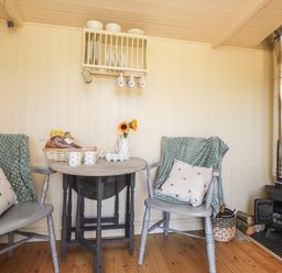 A small dining area with two chairs a round table flowers a basket and a wood stove at The Shepherds Hut at Marley near Barham Kent