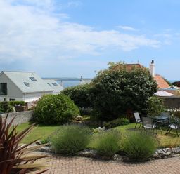A garden with outdoor chairs and table surrounded by bushes and houses near the sea at Robin Hill in Duporth near St Austell