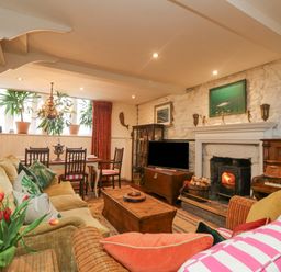 A living room with sofas a fireplace a wooden chest a dining table with chairs plants and a piano at Roncon's Villa in Goldsithney