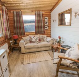 A living room with a beige sofa and pillows wooden rocking chair wooden side tables and curtains at Ingram in Longframlington