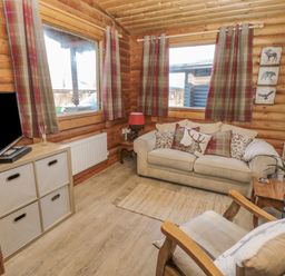 A living room with a beige sofa with cushions a TV on a storage unit and wooden walls at Ingram in Longframlington