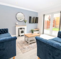 A living room with blue sofas a coffee table a TV mounted on a wall and patio doors at Harbour Place in Wells-Next-The-Sea