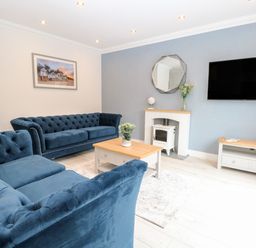 A living room with blue sofas a wooden coffee table a mirror above a fireplace and a wall mounted television at Harbour Place in Wells-Next-The-Sea