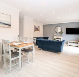 A dining area with a table set for four and a living room with blue sofas and a mounted television at Harbour Place in Wells-Next-The-Sea