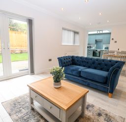 A living area with a blue sofa a wooden coffee table and dining table near a kitchen at Harbour Place in Wells-Next-The-Sea