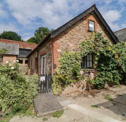 Stone cottage covered with climbing plants and a wooden gate with the name The Holt in Harcombe near Sidford