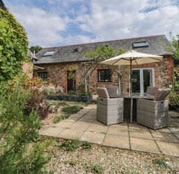 A stone house with slate roof and skylights with a patio table chairs and umbrella in the garden at The Holt Harcombe near Sidford